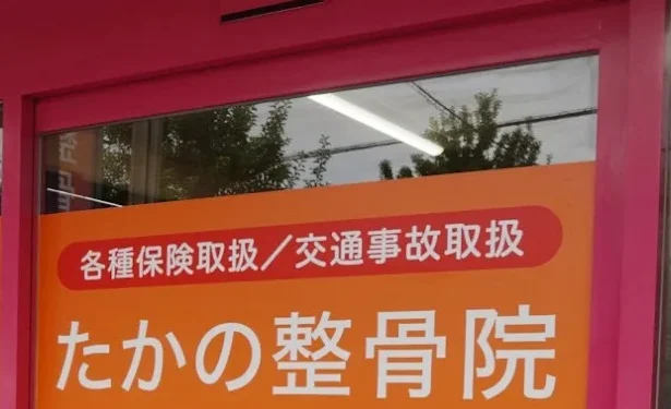 たかの整骨院の入口。ピンク色の枠のガラス戸に、院名を記したオレンジ色の掲示が貼られている